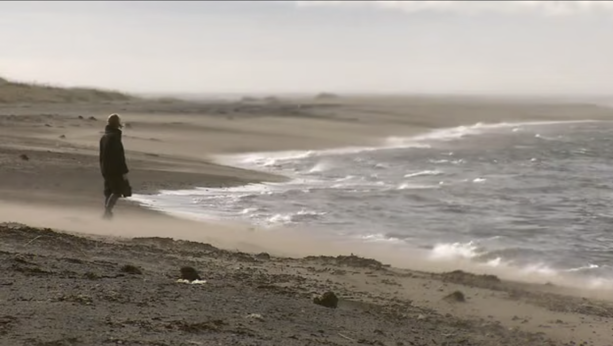 Eine Person mit Mantel an einem Strand