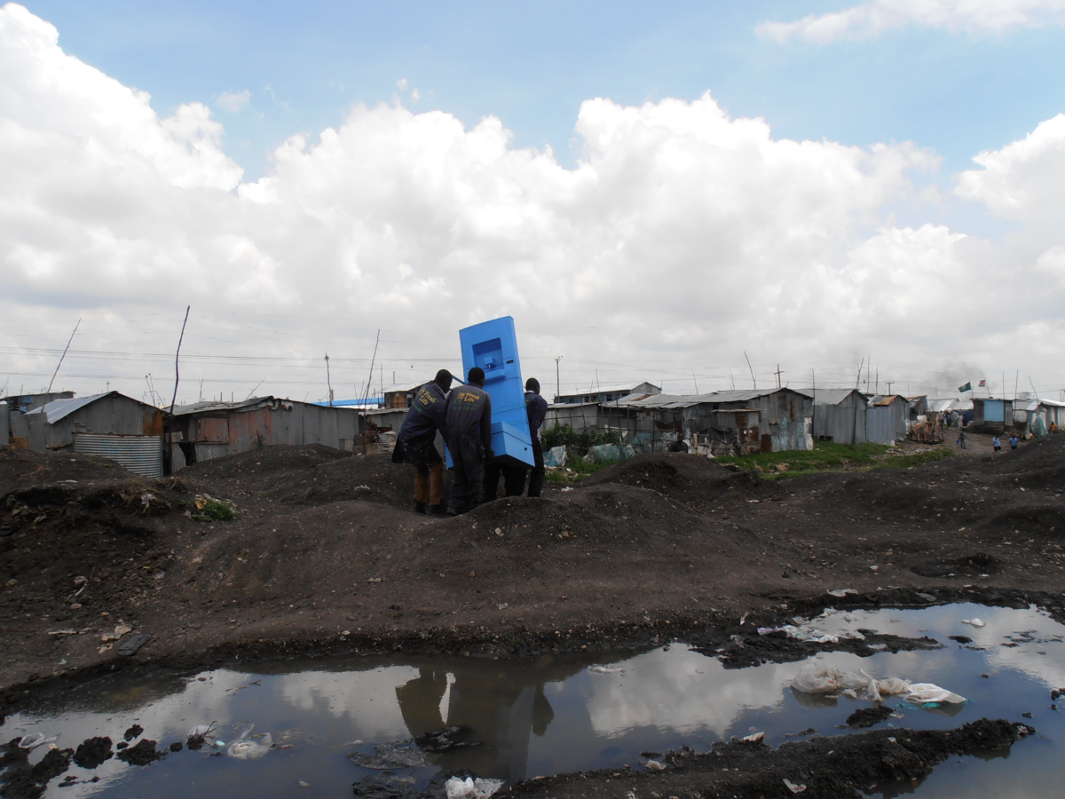 Three people carrying a blue object in a rural area next to a big, dirty puddle