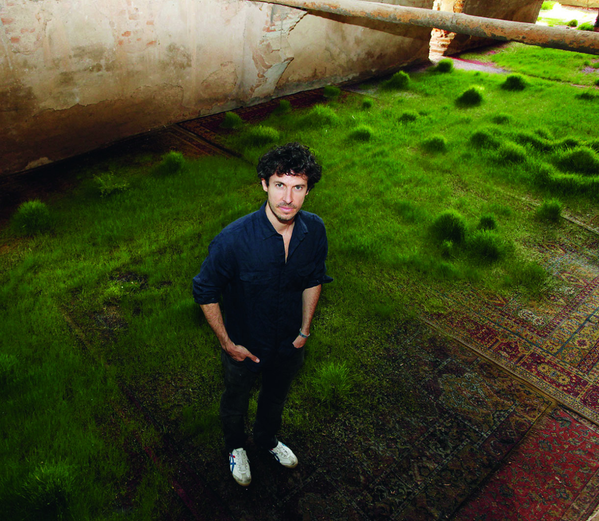 Artist looks at camera above him while standing in his installation