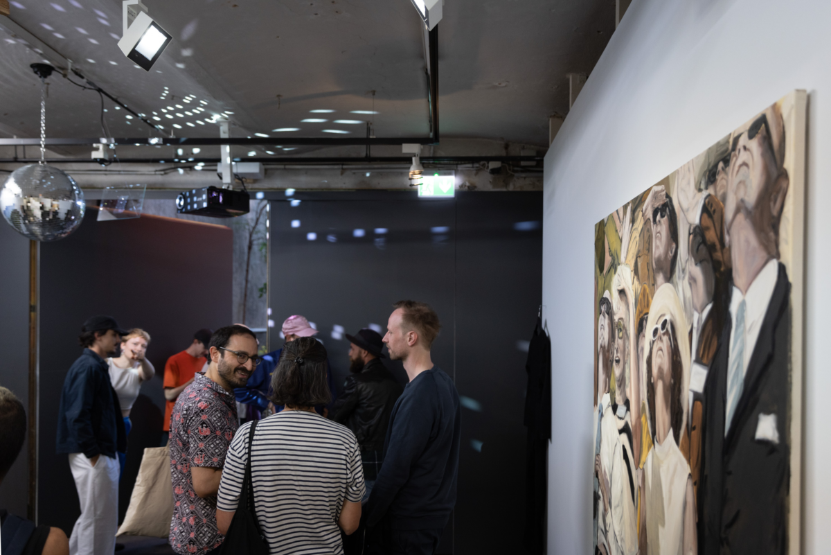 Die Besucher stehen in einem schwach beleuchteten Raum, eine Discokugel hängt von der Decke, Kunstwerke hängen an den Wänden