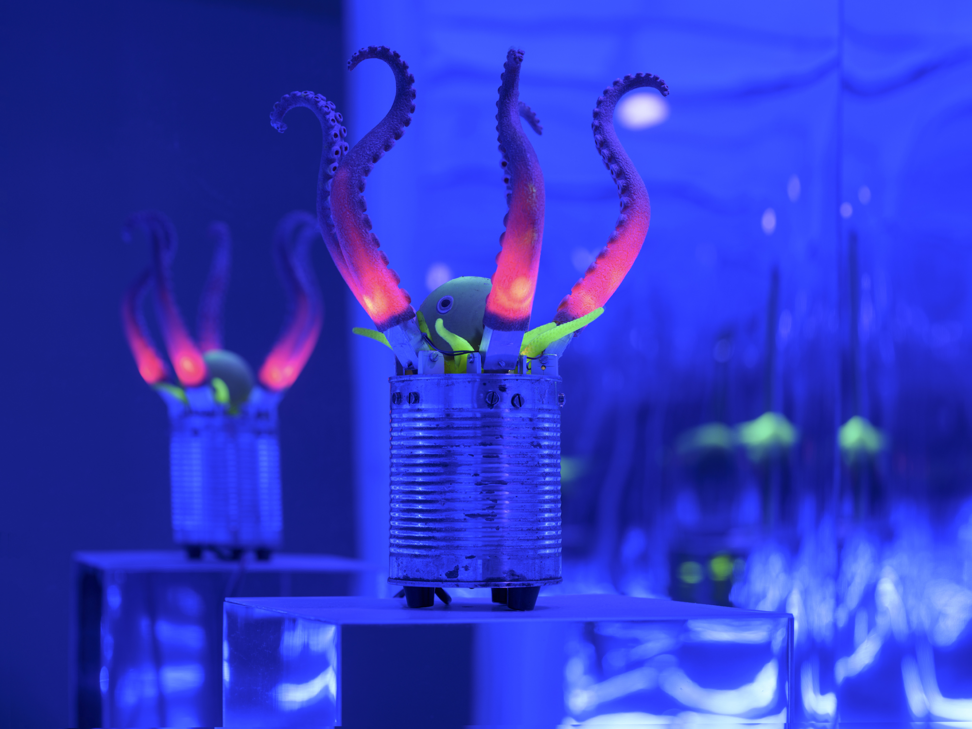 Mechanische Otopusarme ragen aus einer Blechdose auf einem Podest, umgeben von reflektierenden Wänden