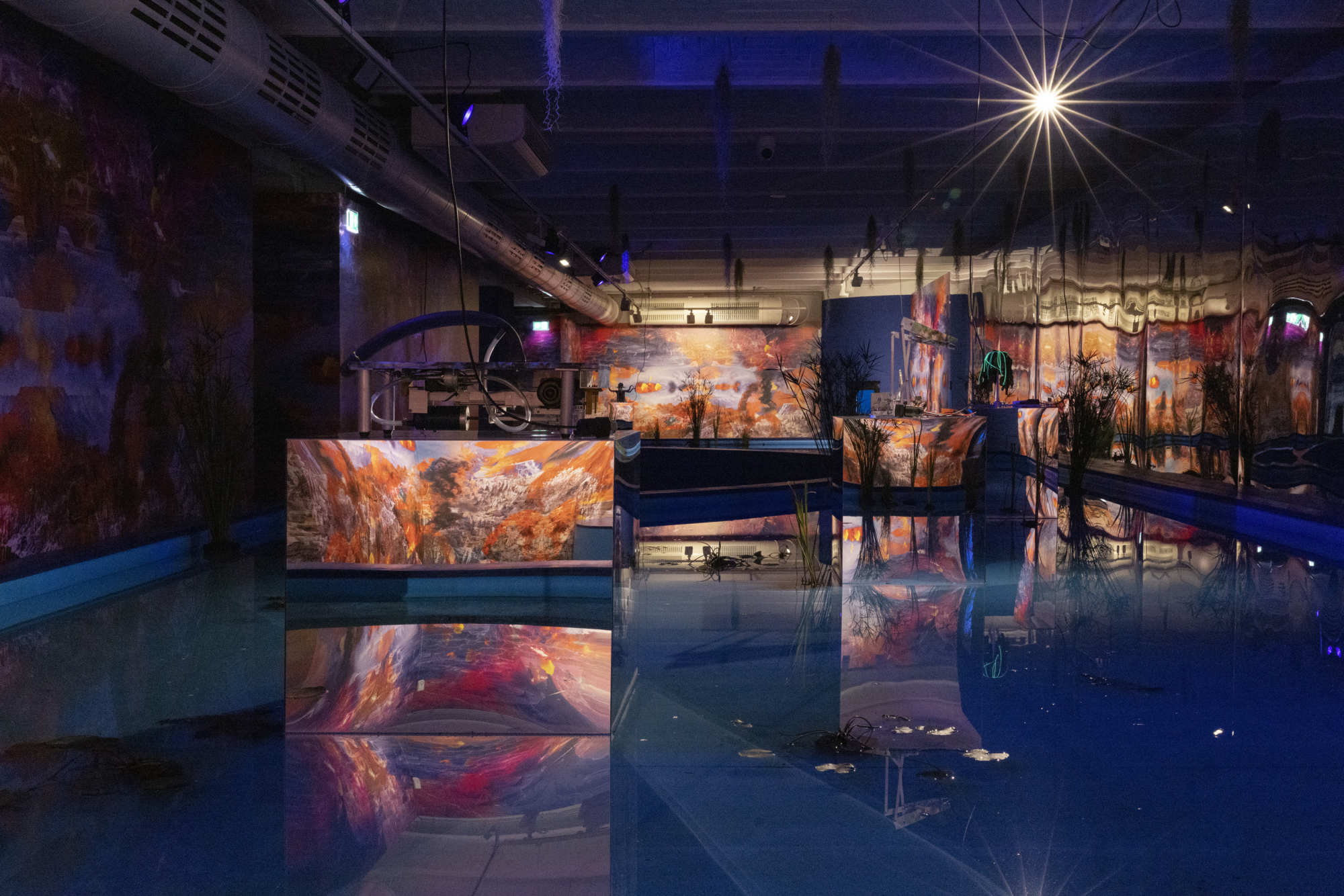 flaches Becken mit rechteckigen, reflektierenden Podesten, auf denen sich Metallskulpturen befinden